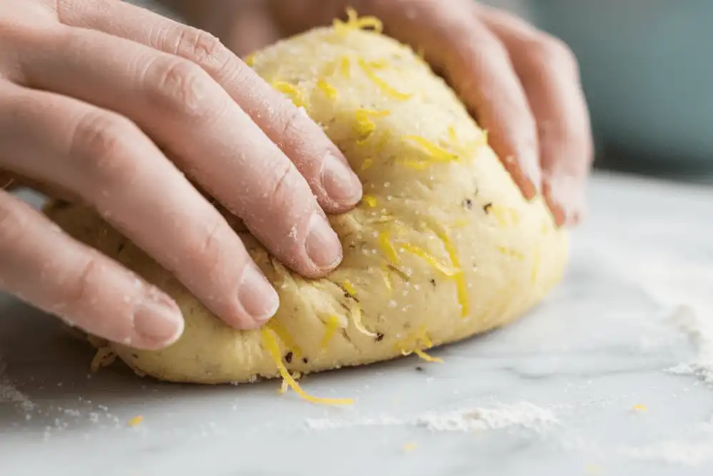Close-up of cookie dough being kneaded with citrus zest and pure vanilla bean specks on a marble pastry board
