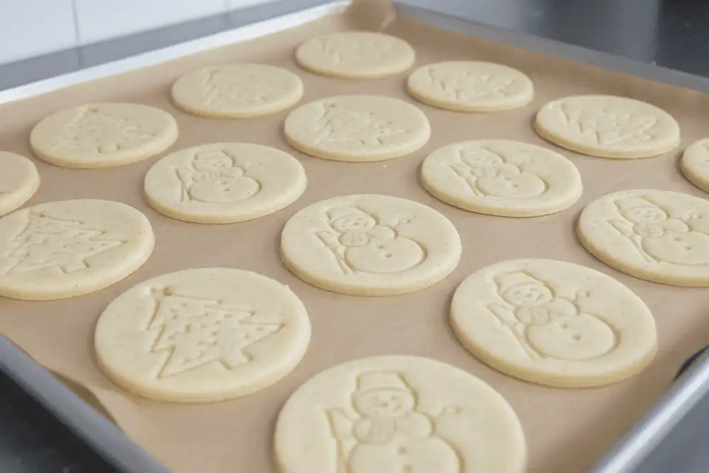 Unbaked pre-cut holiday printed shape cookies arranged on a parchment-lined baking sheet
